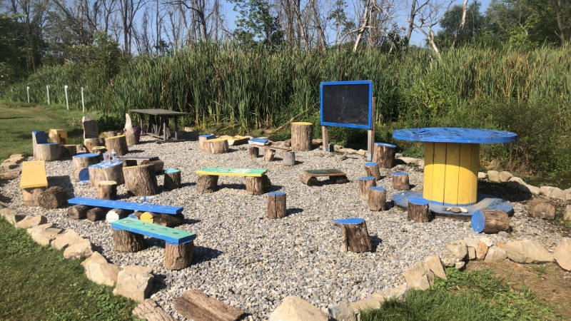 An outdoor classroom with brightly colored log stools and benches.