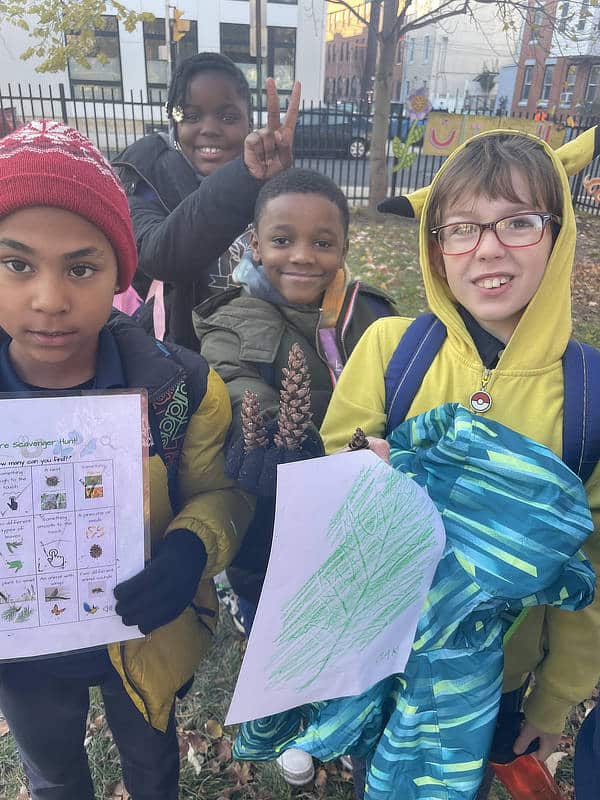 Four elementary schools students with things they found on a nature scavenger hunt.