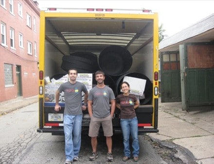 Three people delivering rain barrels from the back of a truck.