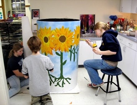 Students painting sunflowers on a rain barrel.