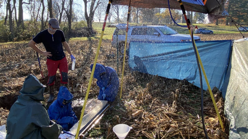 Four scientists perform a rainfall simulation experiment in a no-till cornfield.
