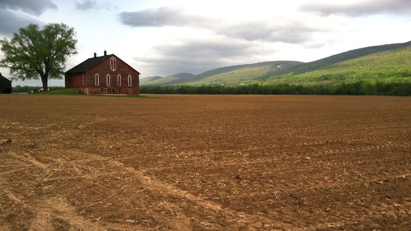 A red building tucked in the middle of a vast tilled field.