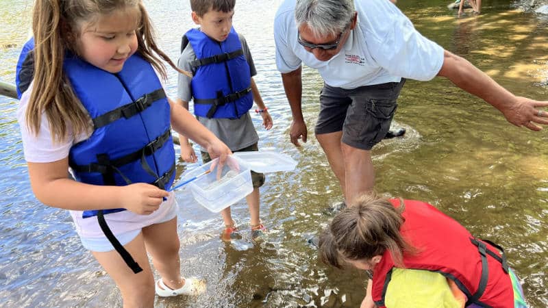 Three children and a man collect stream insects at a Seneca Nation summer camp.