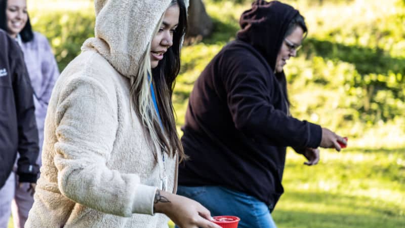 Two Seneca Nation women run a foot race while holding cups of water.