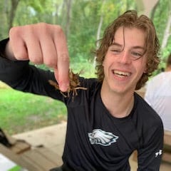 A smiling student holds a crayfish.