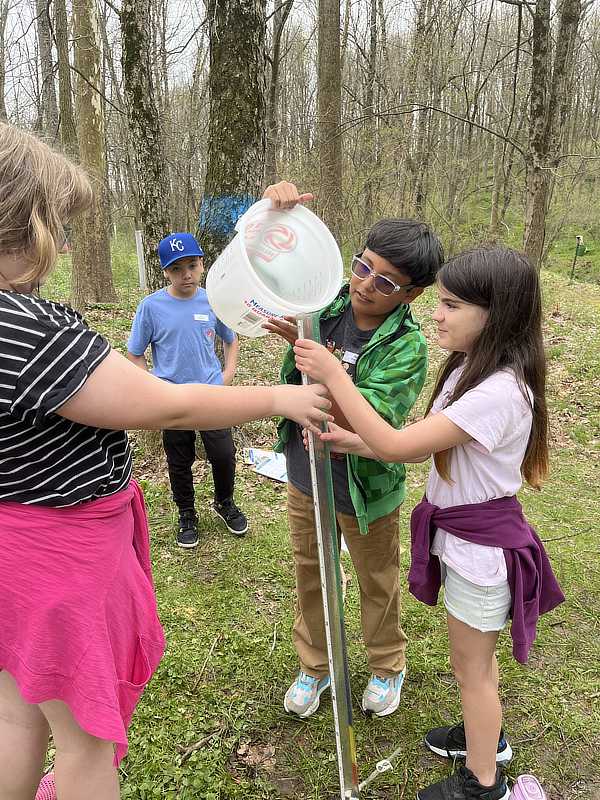 A group of students pours a stream water sample into a long clear tube.