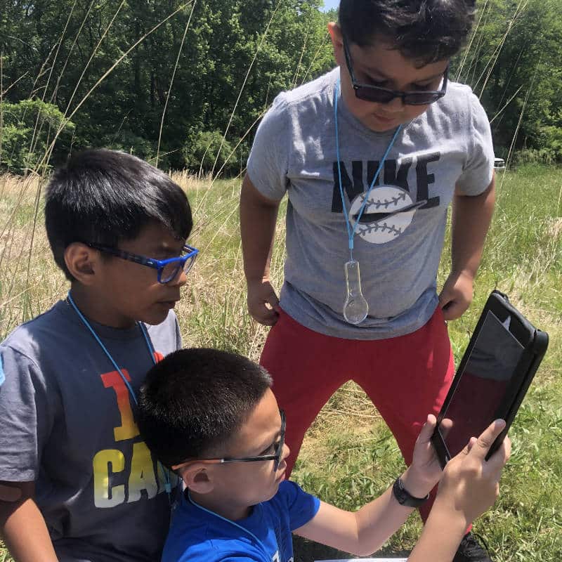 Three elementary school students look at a tablet computer while outdoors.