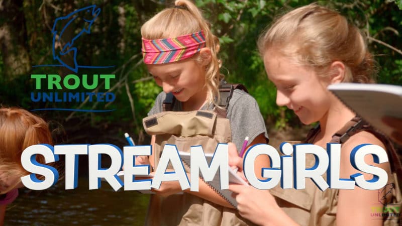 Two girls wearing waders record stream study data in notebooks.