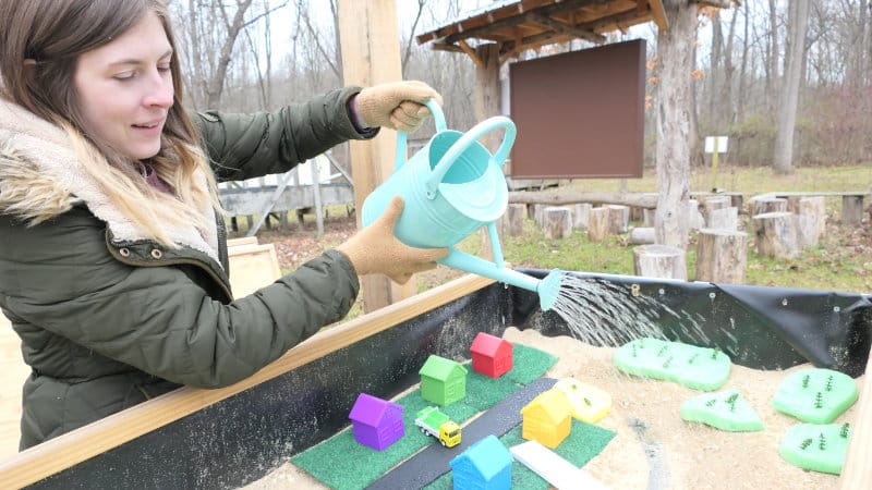 A woman sprinkles water from a watering can onto a watershed modeling table.