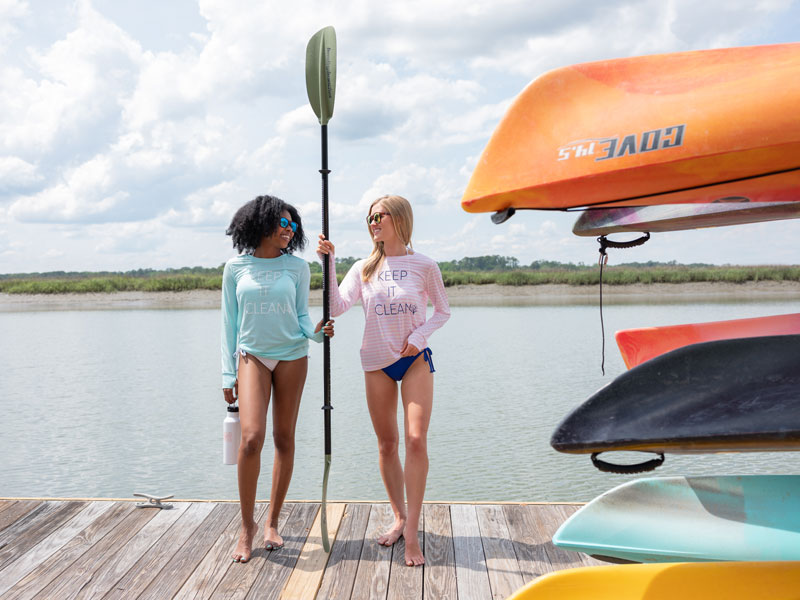 Two women stand on a dock next to a rack of kayaks.