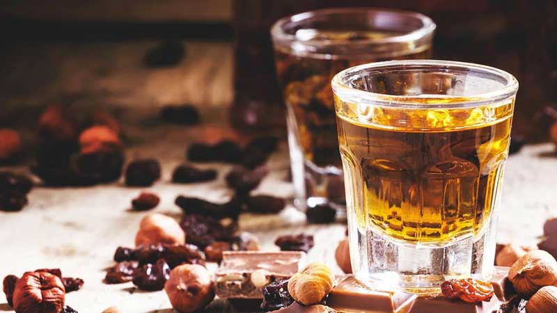 Photo of two shots of whiskey surrounded by nuts and chocolate