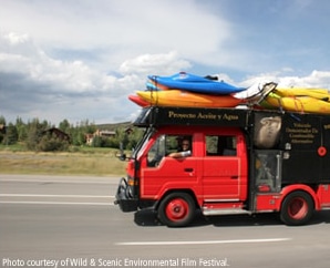 A red truck carrying kayaks travels on a highway.