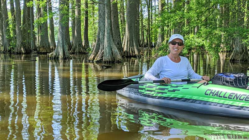 A woman kayaks near a stand of bald cypress trees.